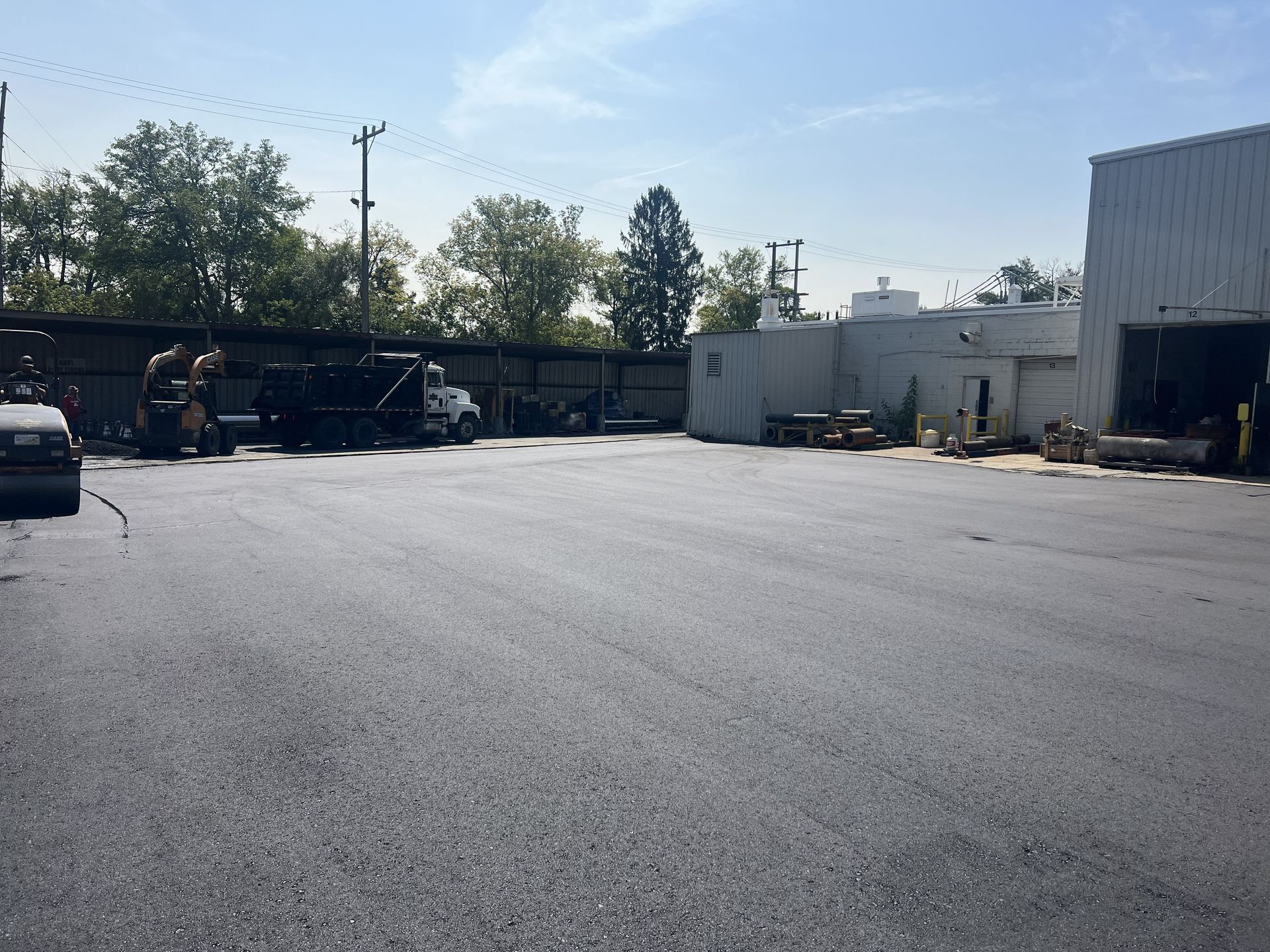Wide empty asphalt lot beside industrial buildings under a bright sky