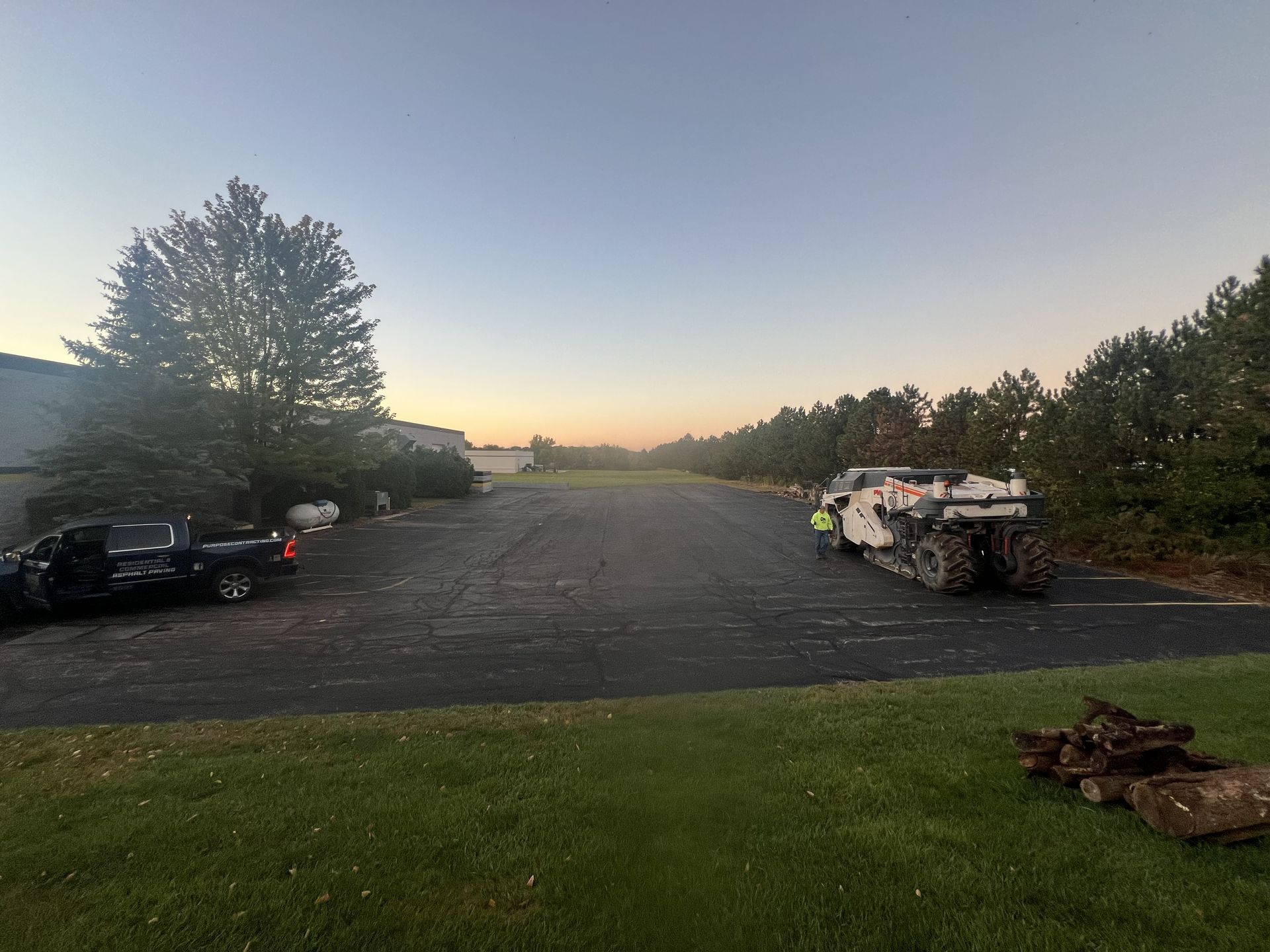 Empty parking lot at dusk with parked cars, trees, and a low sunset glow over the horizon