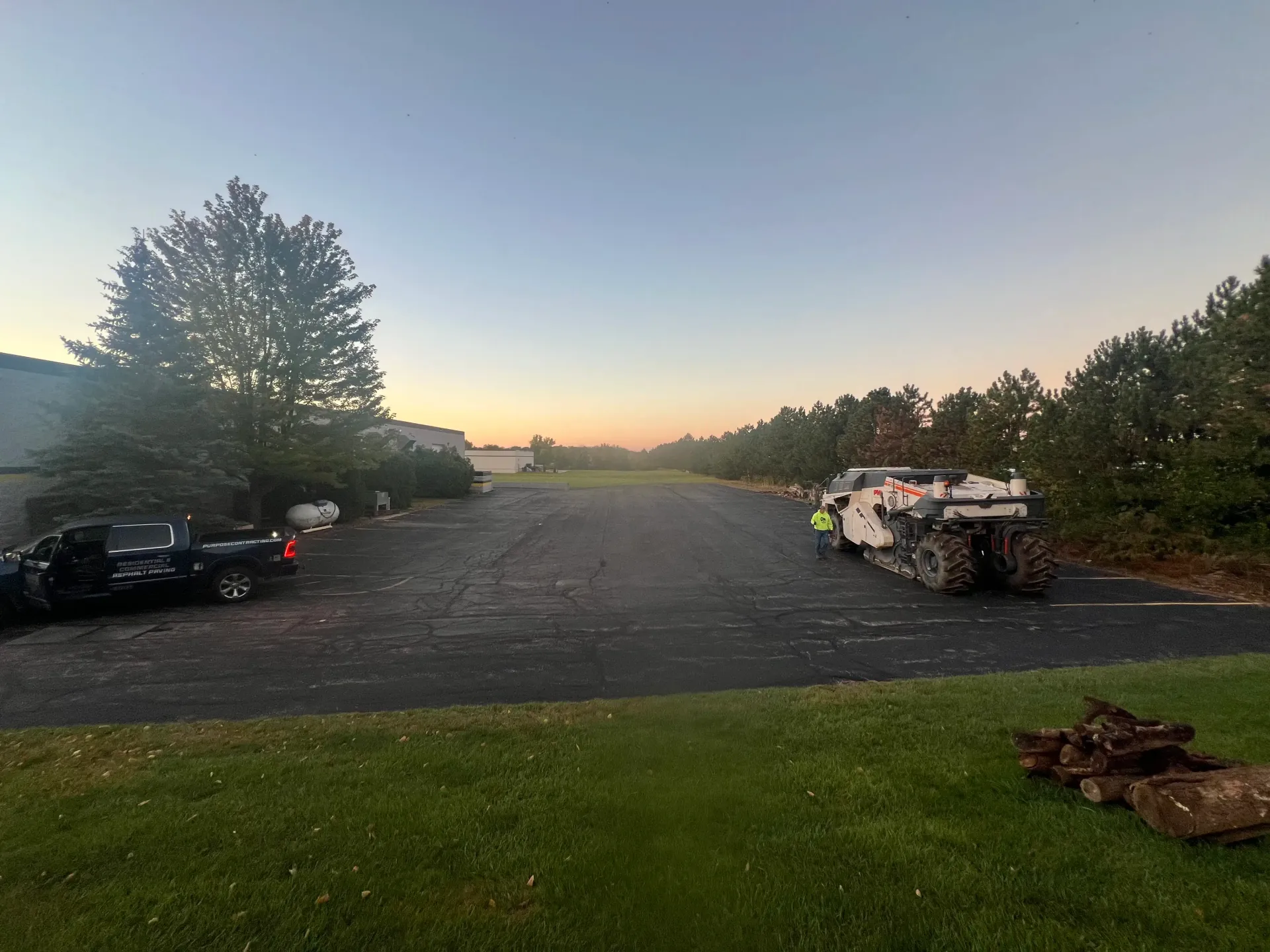 Sunrise over a gravel lot with parked cars and trucks, trees lining the edges, and grass in the foreground