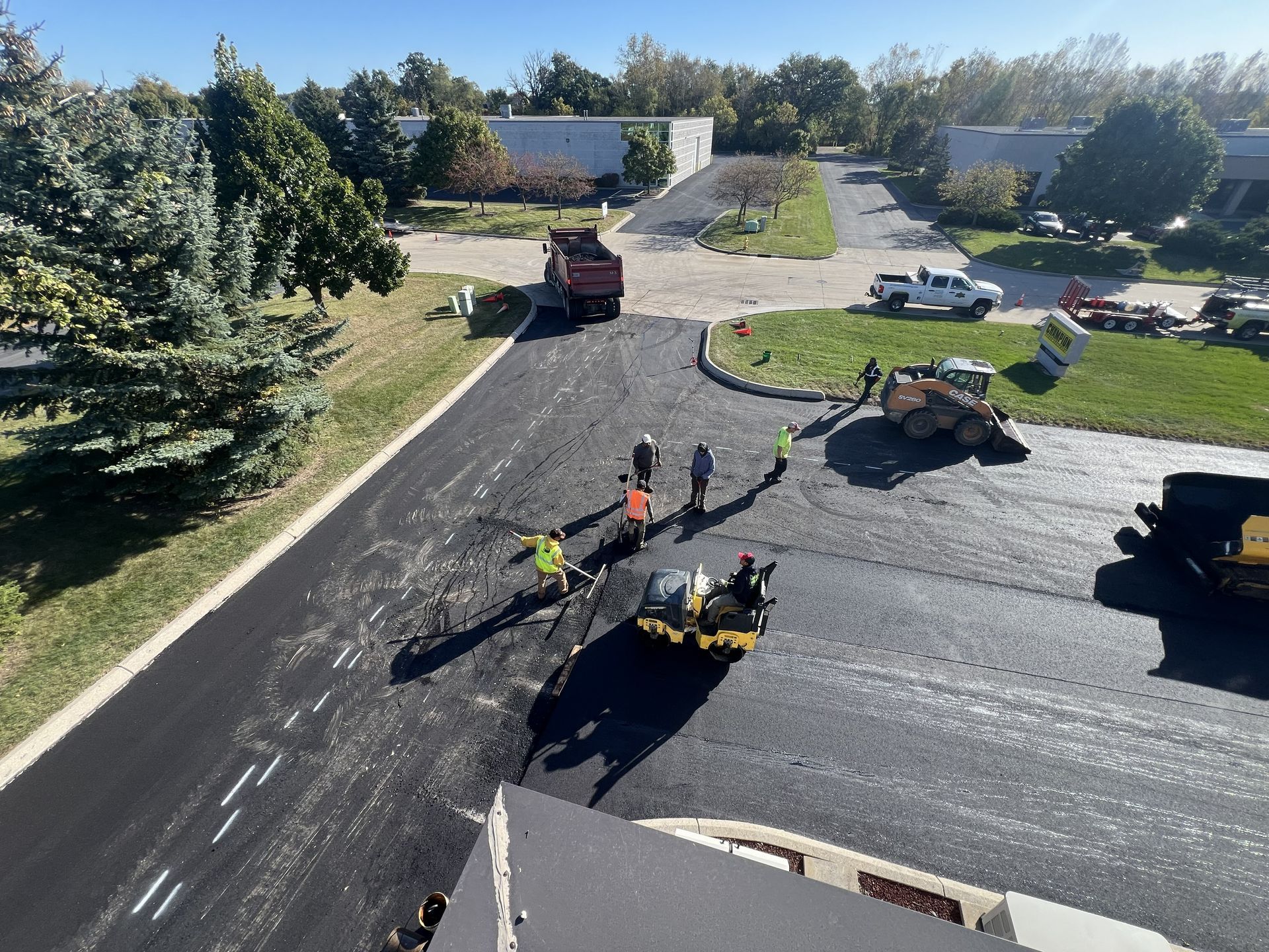 Road crew in high-visibility vests working on a freshly paved parking lot near a dump truck and equipment