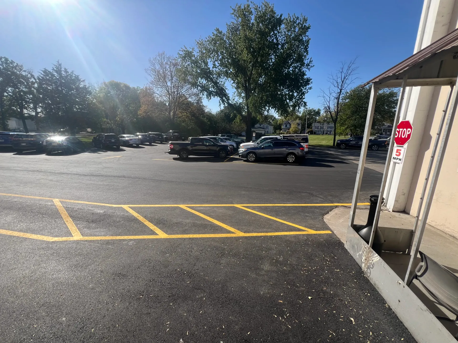 Sunlit parking lot with parked cars, yellow no-parking markings, and a building entrance on the right
