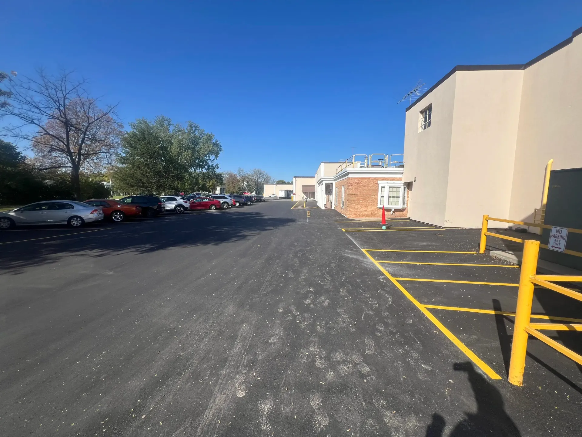 Empty parking lot beside beige buildings, with yellow railings and a clear blue sky.