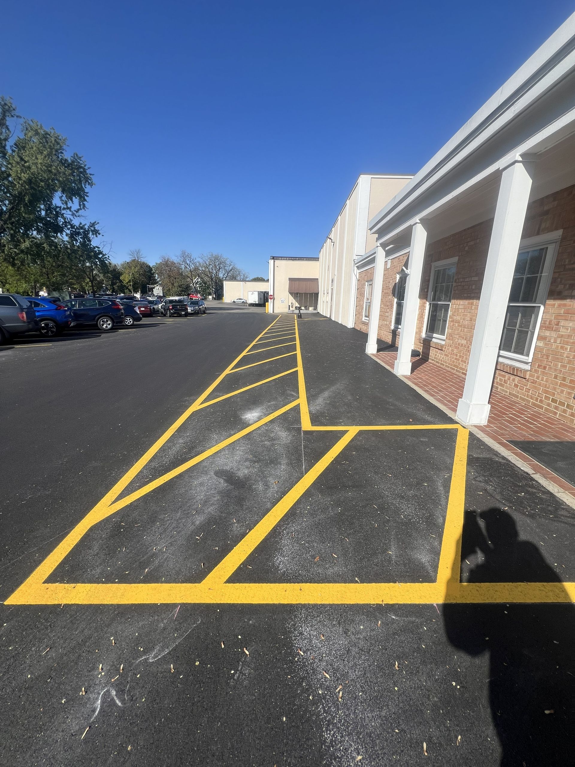 Outdoor building entrance with yellow-striped no-parking zone, brick walkway, and parked cars under a blue sky