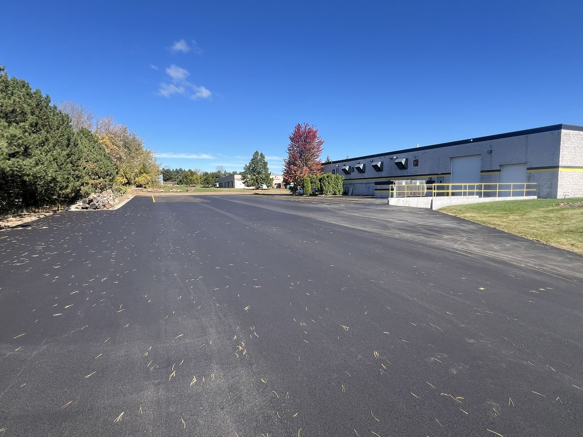 Empty paved lot beside a long gray building under a clear blue sky