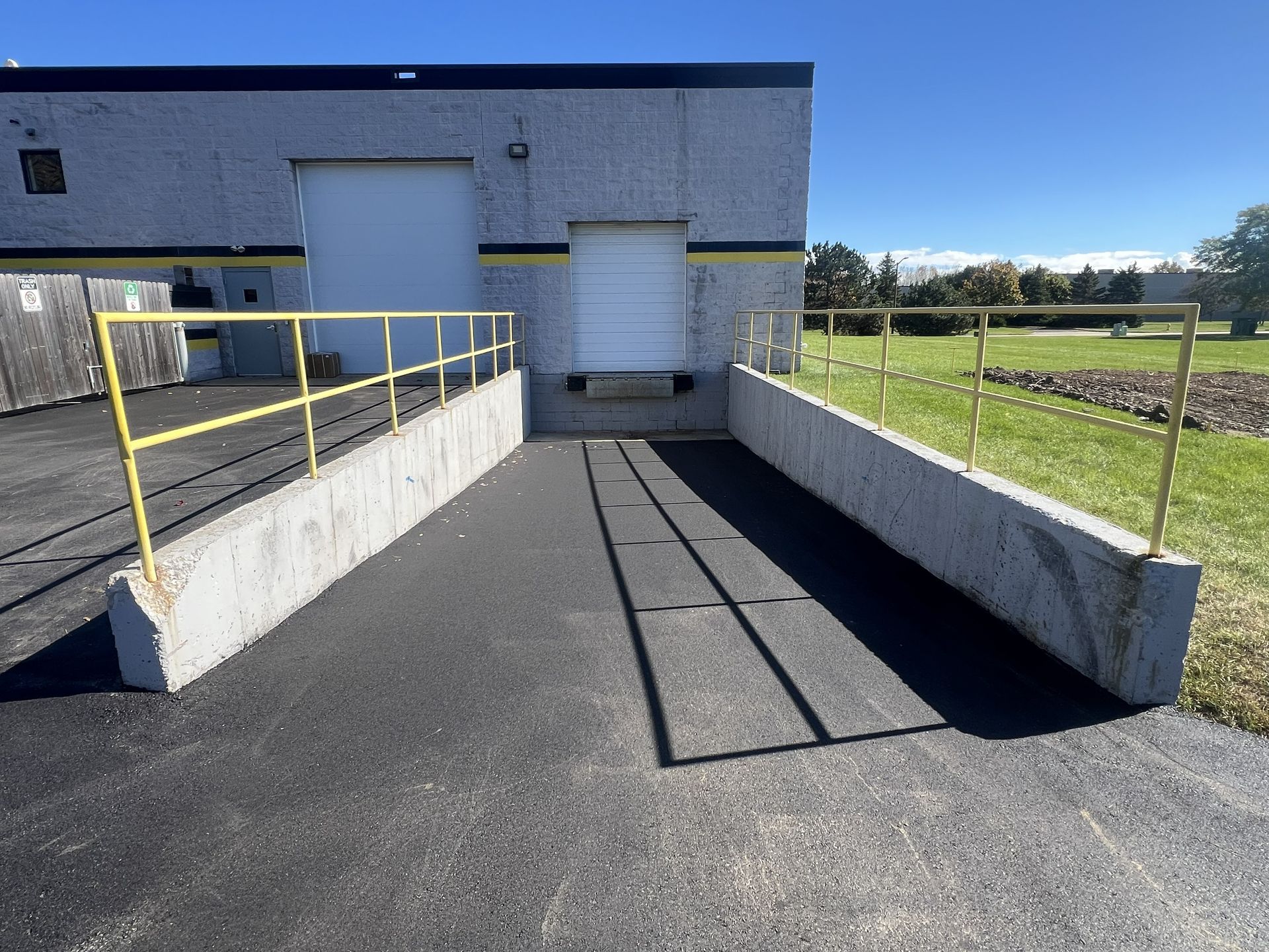 Concrete loading ramp with yellow railings leading to a warehouse loading dock under a clear sky