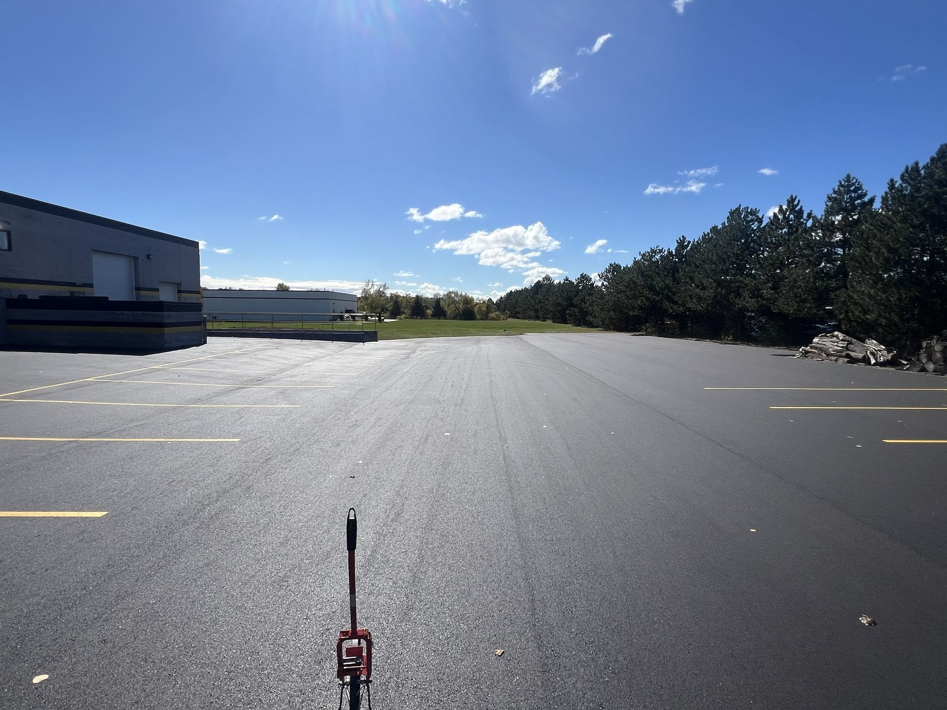 Empty paved lot beside a building under a blue sky, viewed from a low angle with a small tool in the foreground