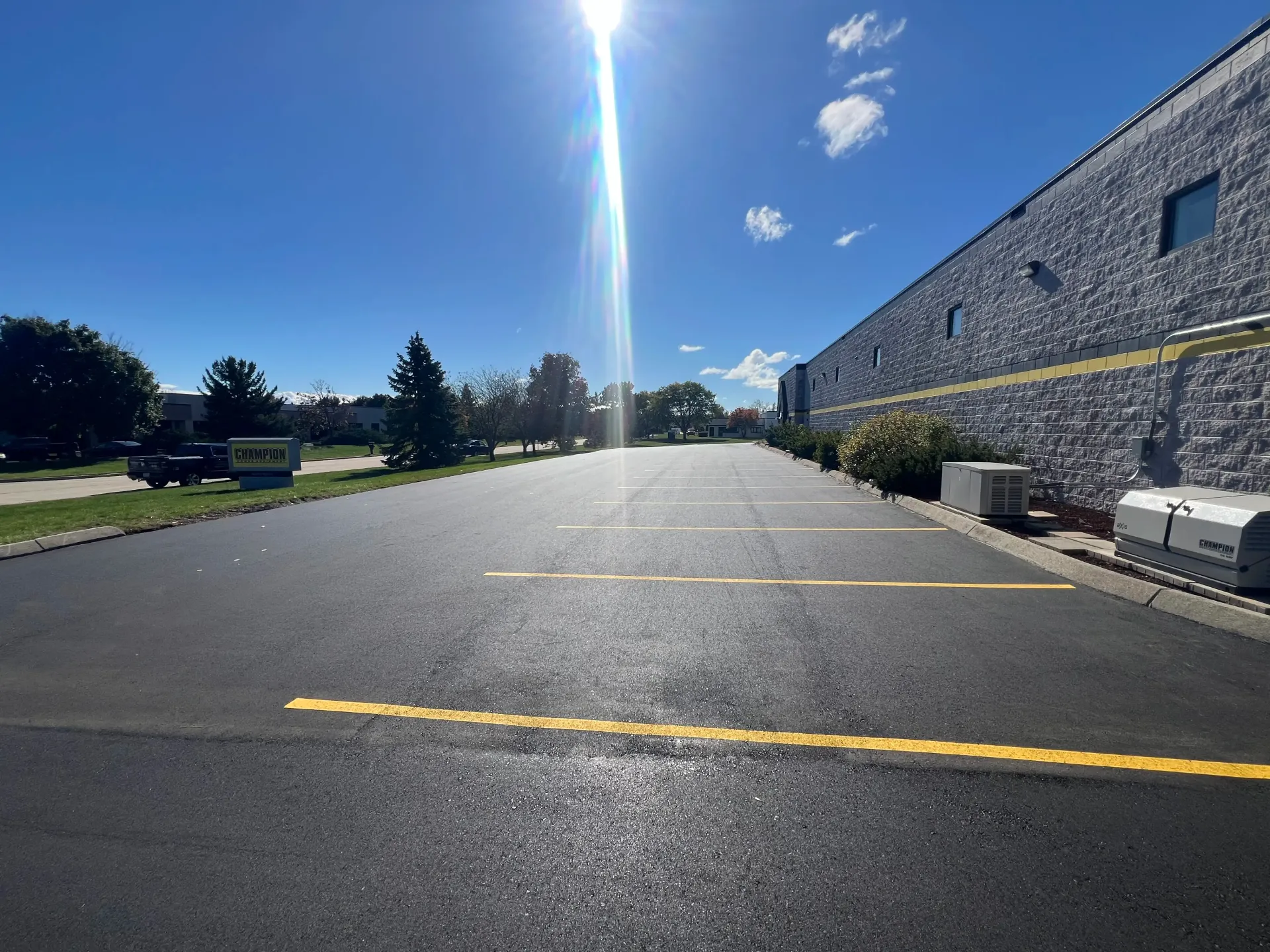 Empty parking lot beside a stone building under bright blue sky with sun glare and painted parking lines