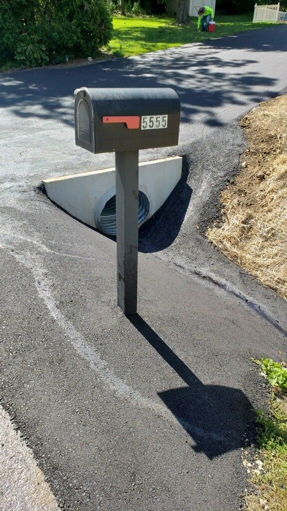 Mailbox beside a curbside drainage hole in a paved driveway