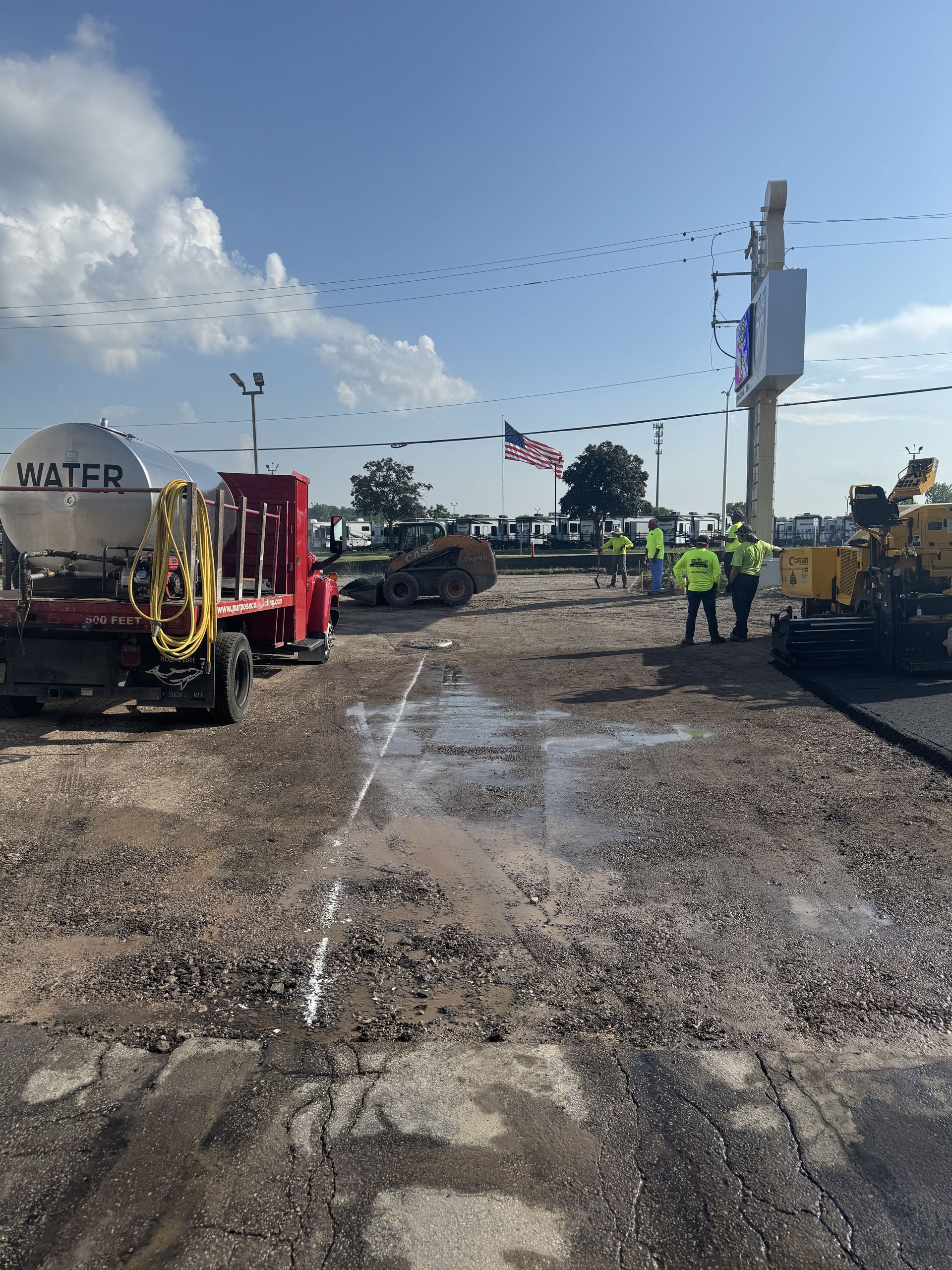 Roadwork site with excavators, workers in high-visibility vests, and a damaged road surface under a clear sky