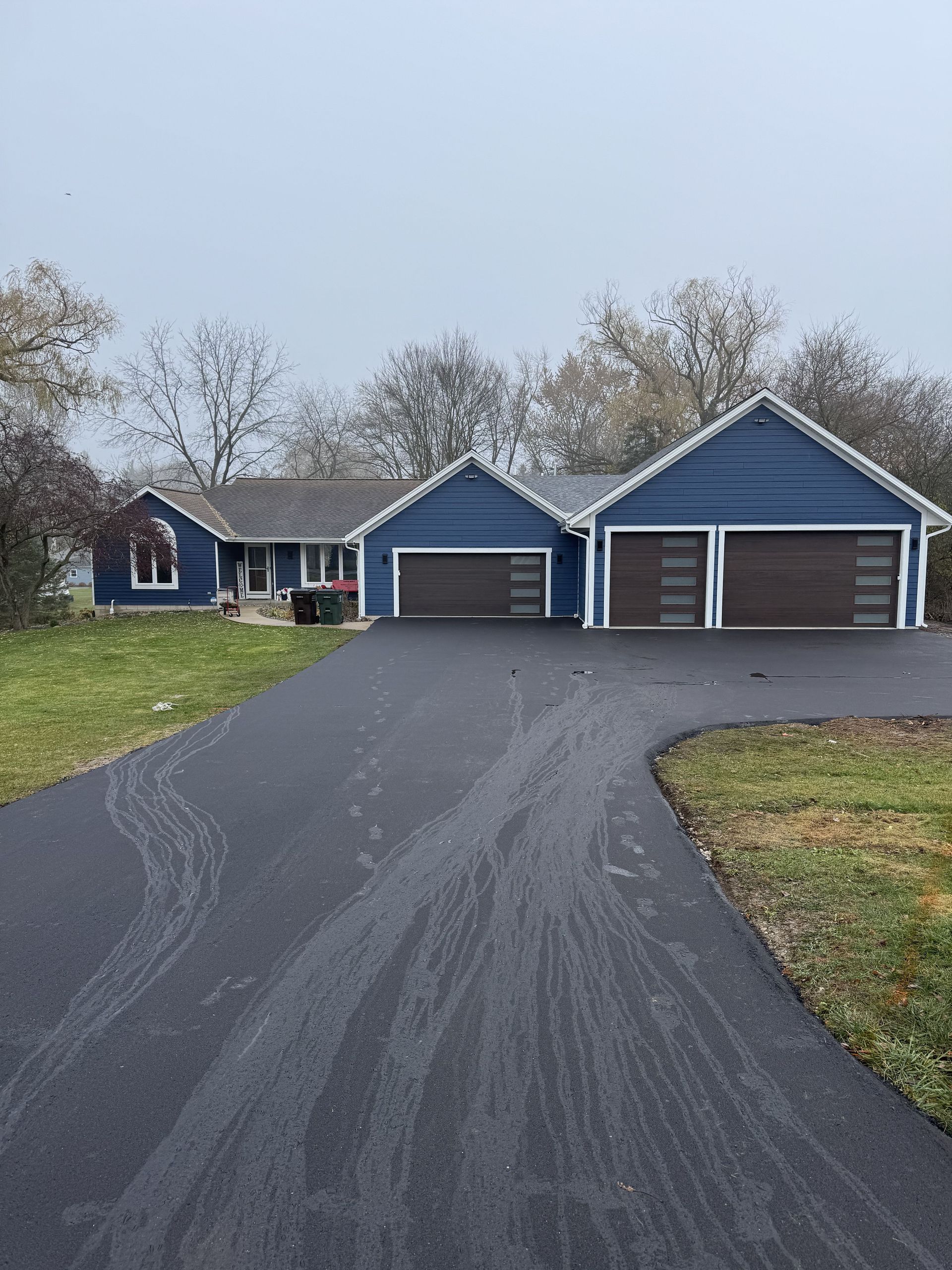 Blue house and three-car garage at the end of a curved asphalt driveway on a cloudy day