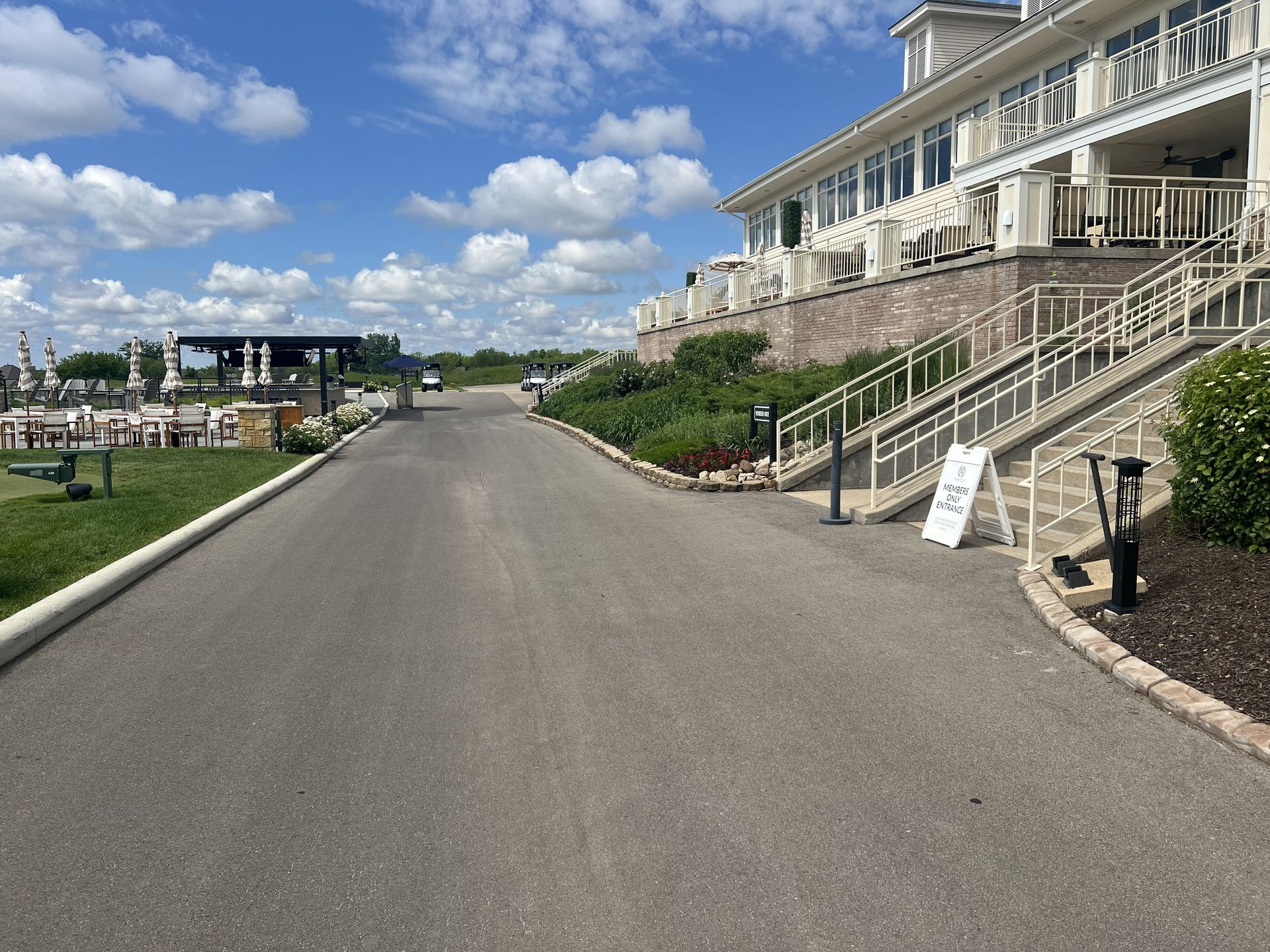 Wide paved driveway beside a grand white building, with stairs, lawn, and blue sky with clouds.