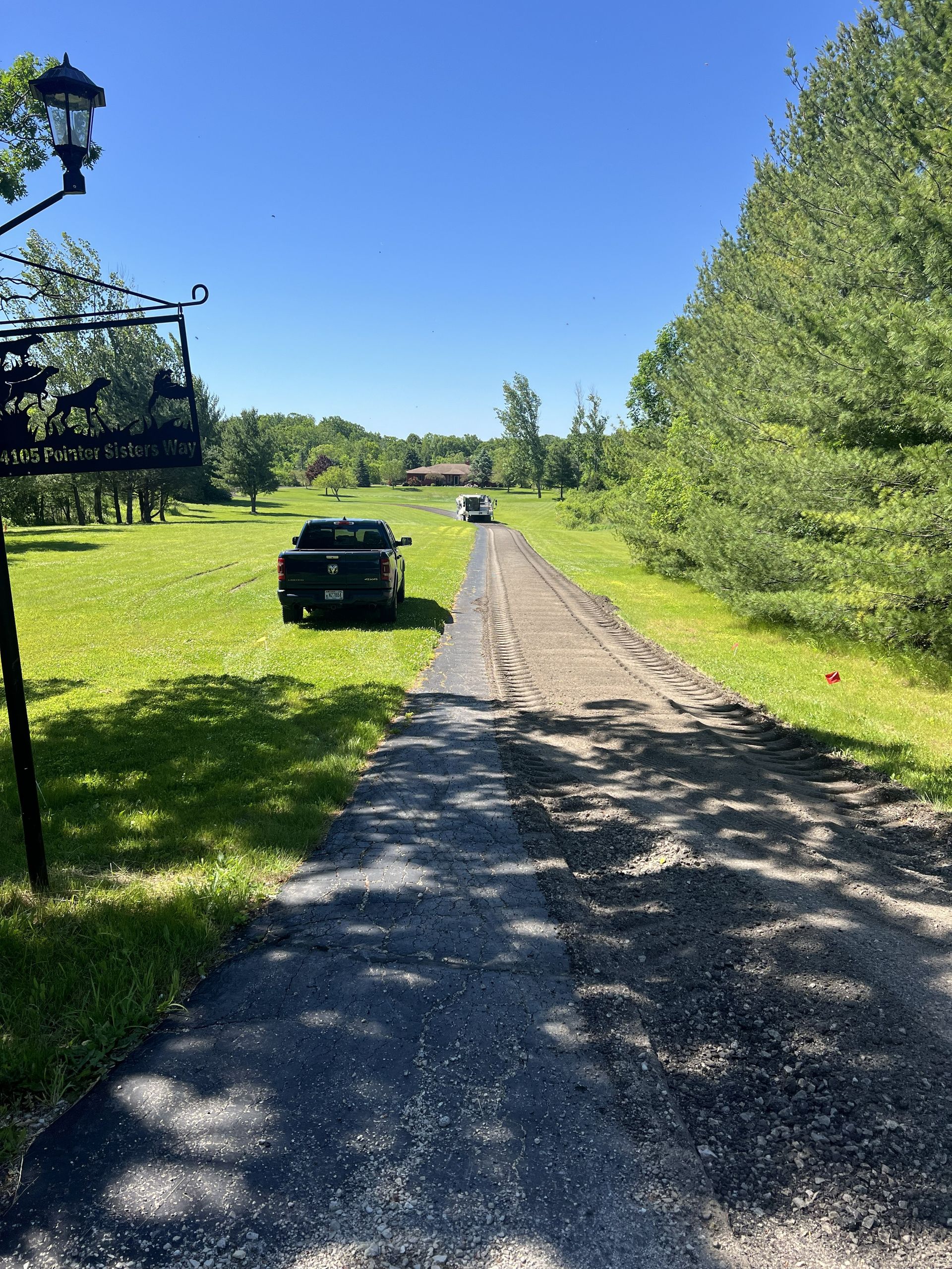 Gravel road through a green park on a sunny day, with cars parked along the left side.
