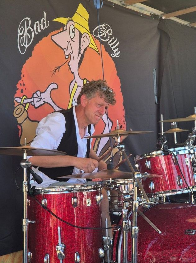Een drummer bespeelt een rood drumstel op het podium, met een