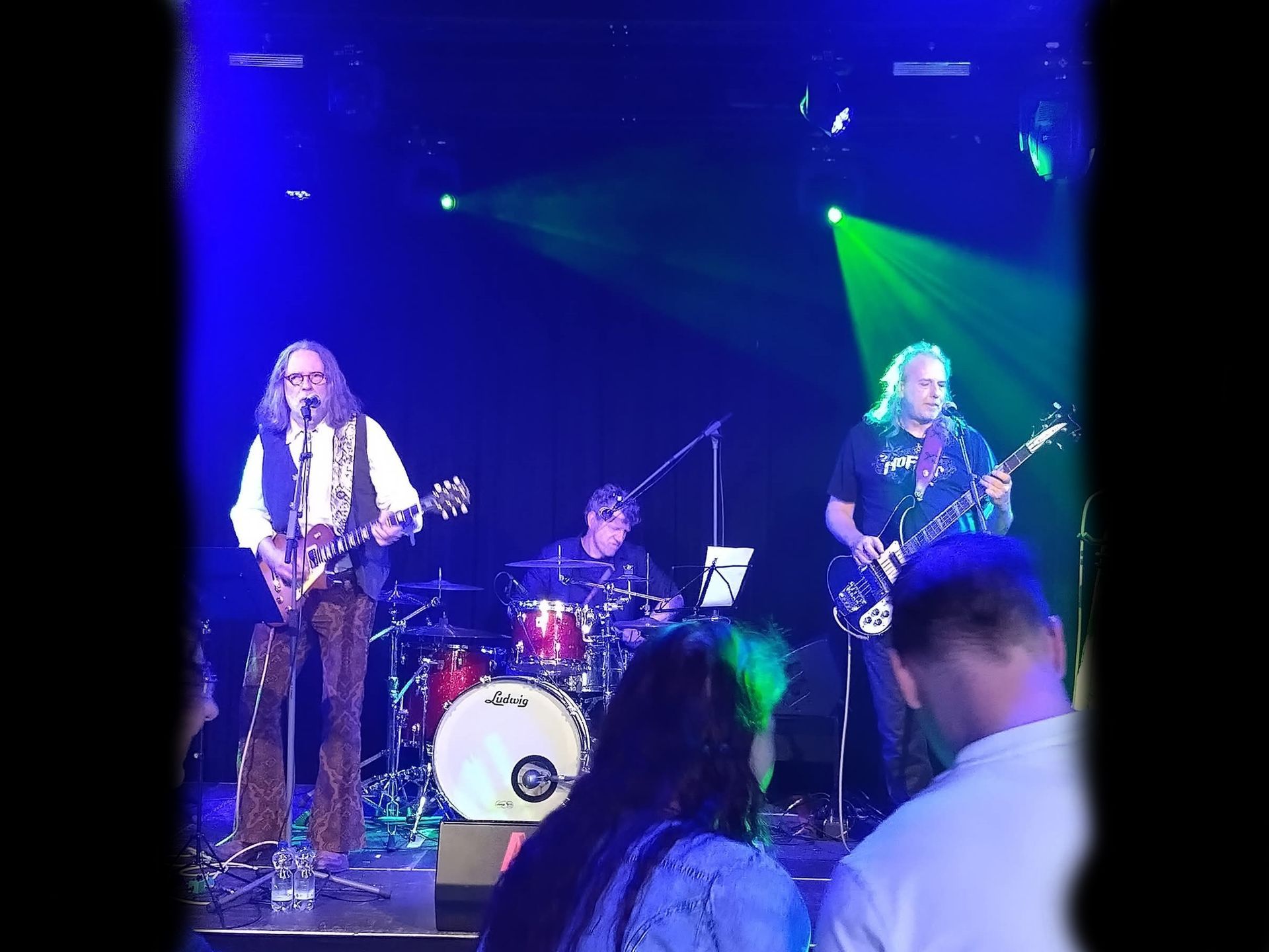Band treedt live op het podium op onder blauwe en groene podiumverlichting.
