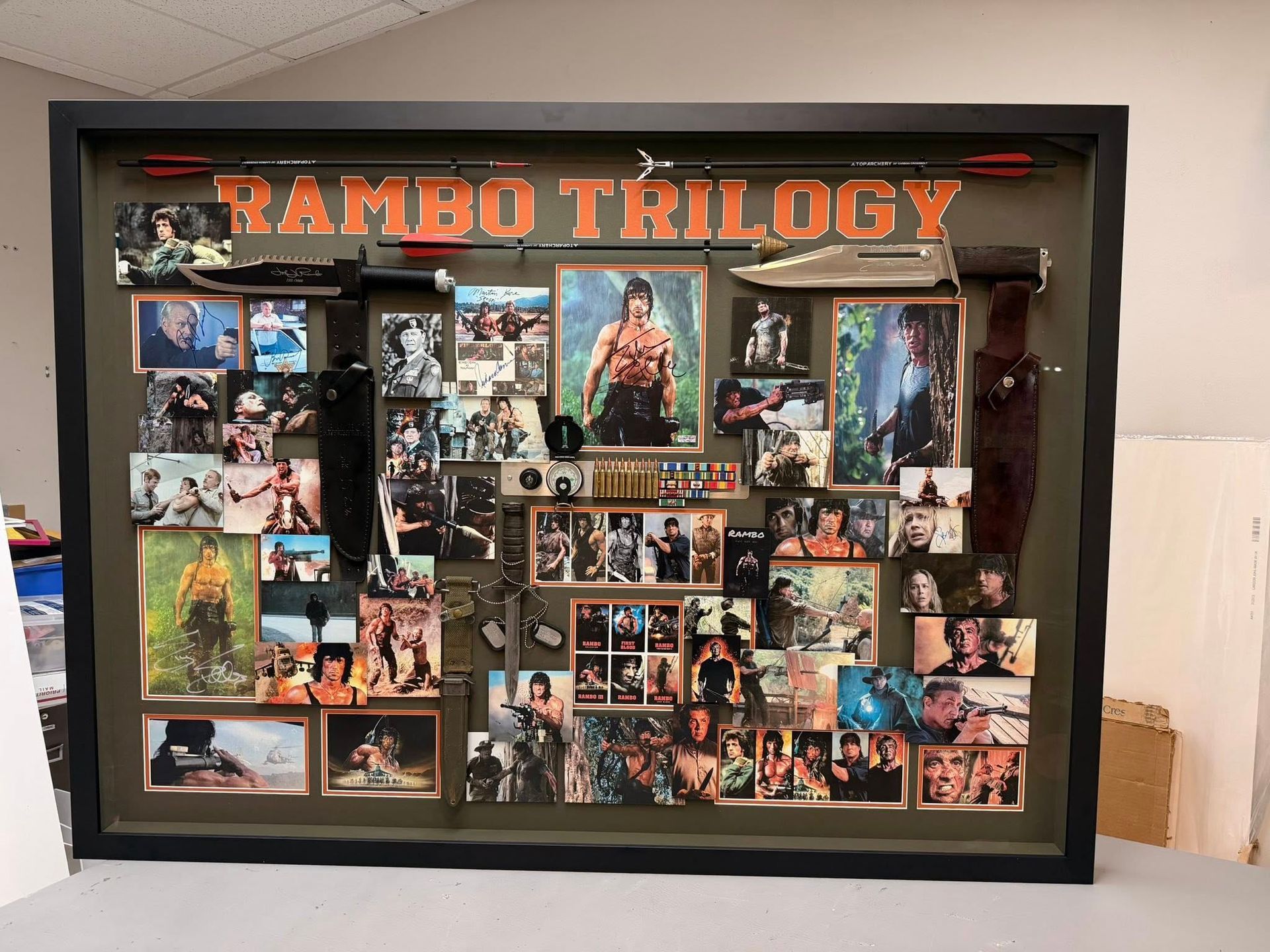Framed Rambo Trilogy collage with movie stills and posters on a shelf against a white wall