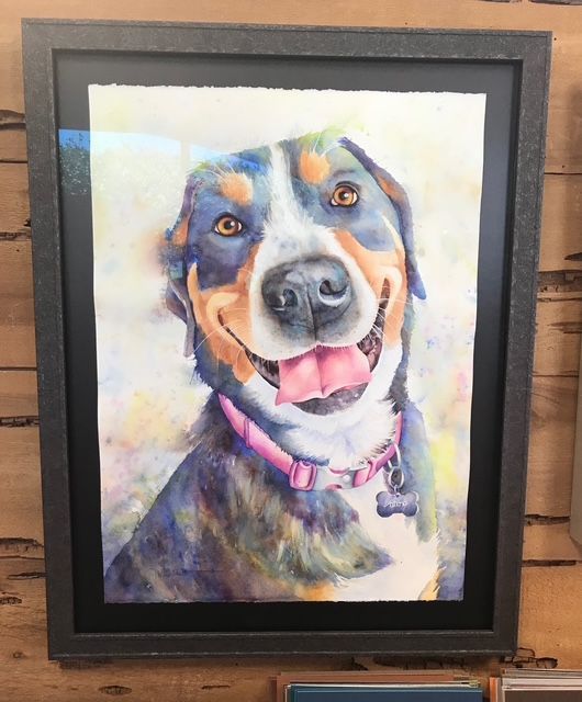 Framed watercolor portrait of a smiling tricolor dog with a pink collar on a brick wall.