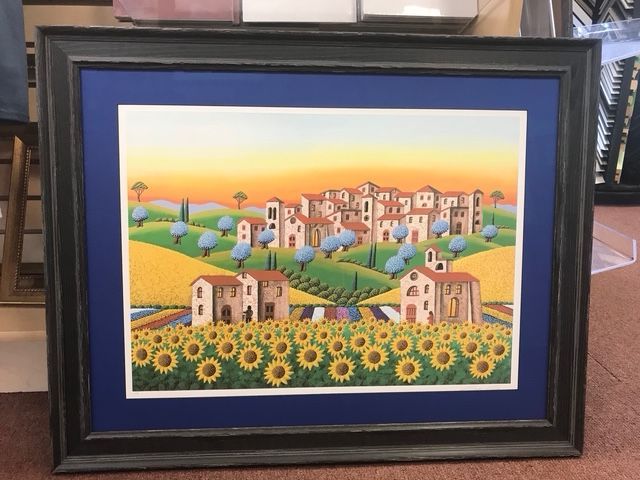 Framed colorful painting of a sunny village landscape with houses, hills, and sunflowers