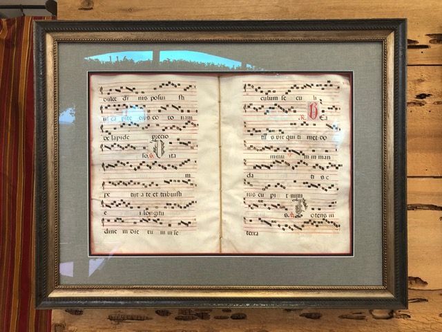 Framed open sheet music displayed behind glass on a wood wall