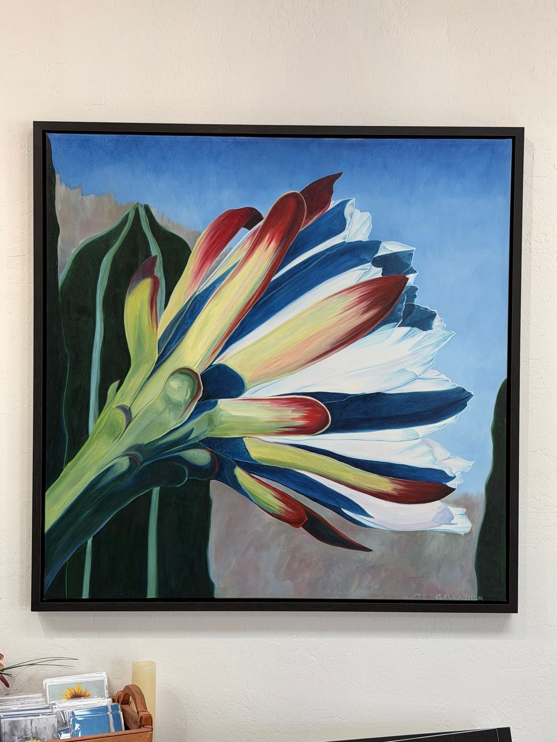 Framed painting of a pink hibiscus flower with green leaves against a blue background.