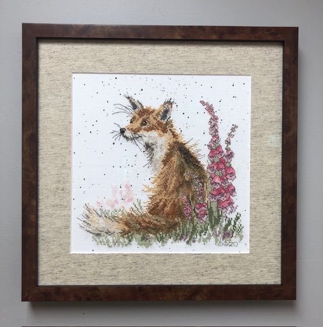Framed watercolor of a fox in grass beside pink flowers on a beige textured background