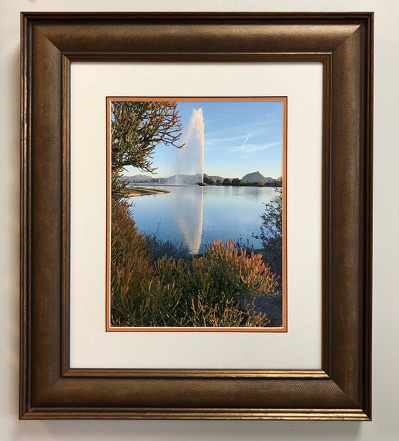 Framed landscape photo of a lake with a fountain, trees, and blue sky