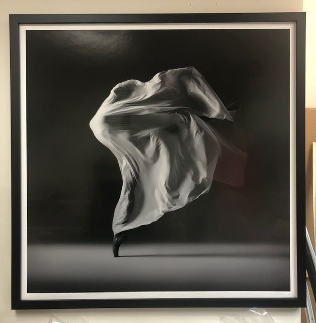 Black-and-white abstract fabric sculpture floating in a black frame against a light wall