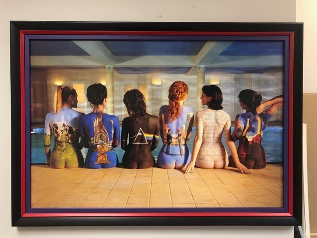 Six seated figures viewed from behind in a colorful framed painting against a warm indoor backdrop.
