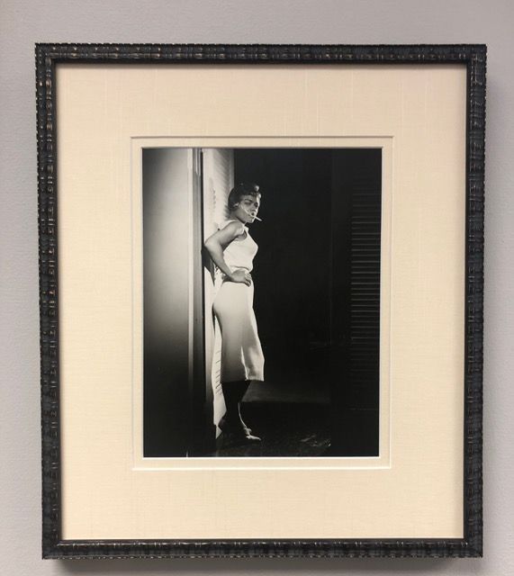 Black-and-white portrait of a woman leaning in a doorway, framed in a beige mat and dark frame.
