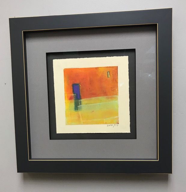 Framed abstract painting with orange, yellow, and blue shapes on a gray wall