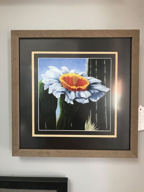 Framed painting of a white flower with an orange center on a black background hanging on a wall