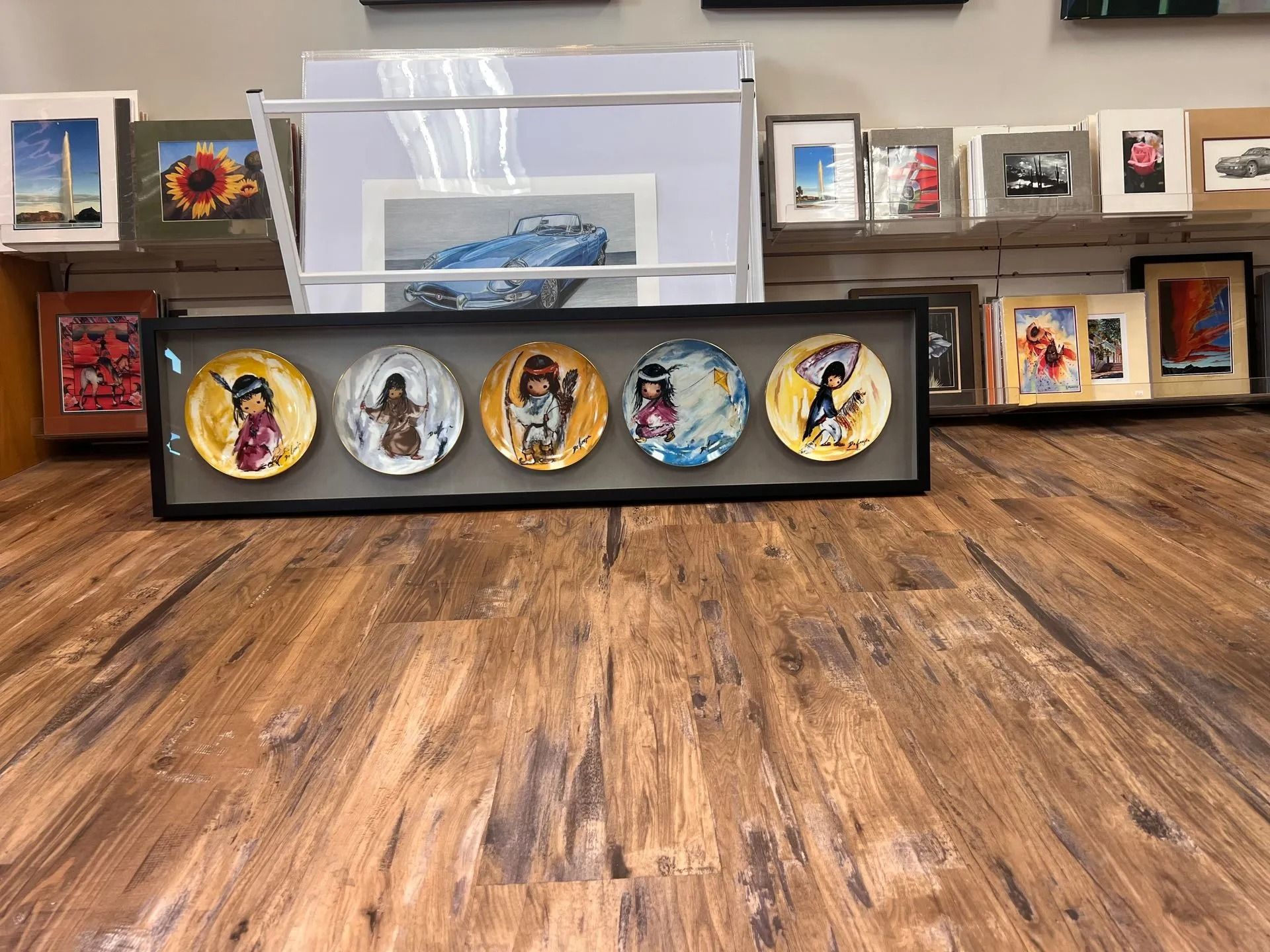 Framed religious portrait display on a wooden floor with a transparent tray behind it and wall art in the background