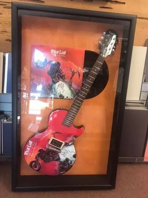 Framed red electric guitar display with a Black Sabbath album cover in the background