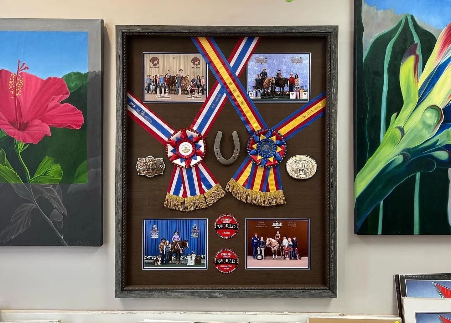 Framed military medals and ribbons displayed between two flower paintings on a wall.