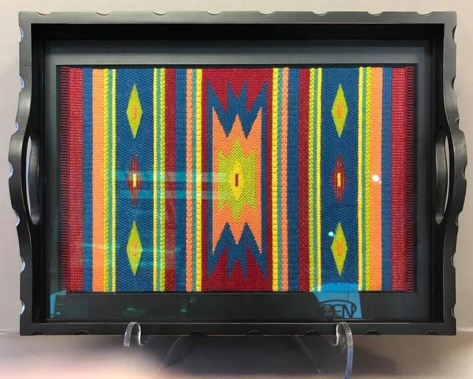 Colorful geometric textile art with vertical stripes, diamonds, and zigzag patterns in a black frame