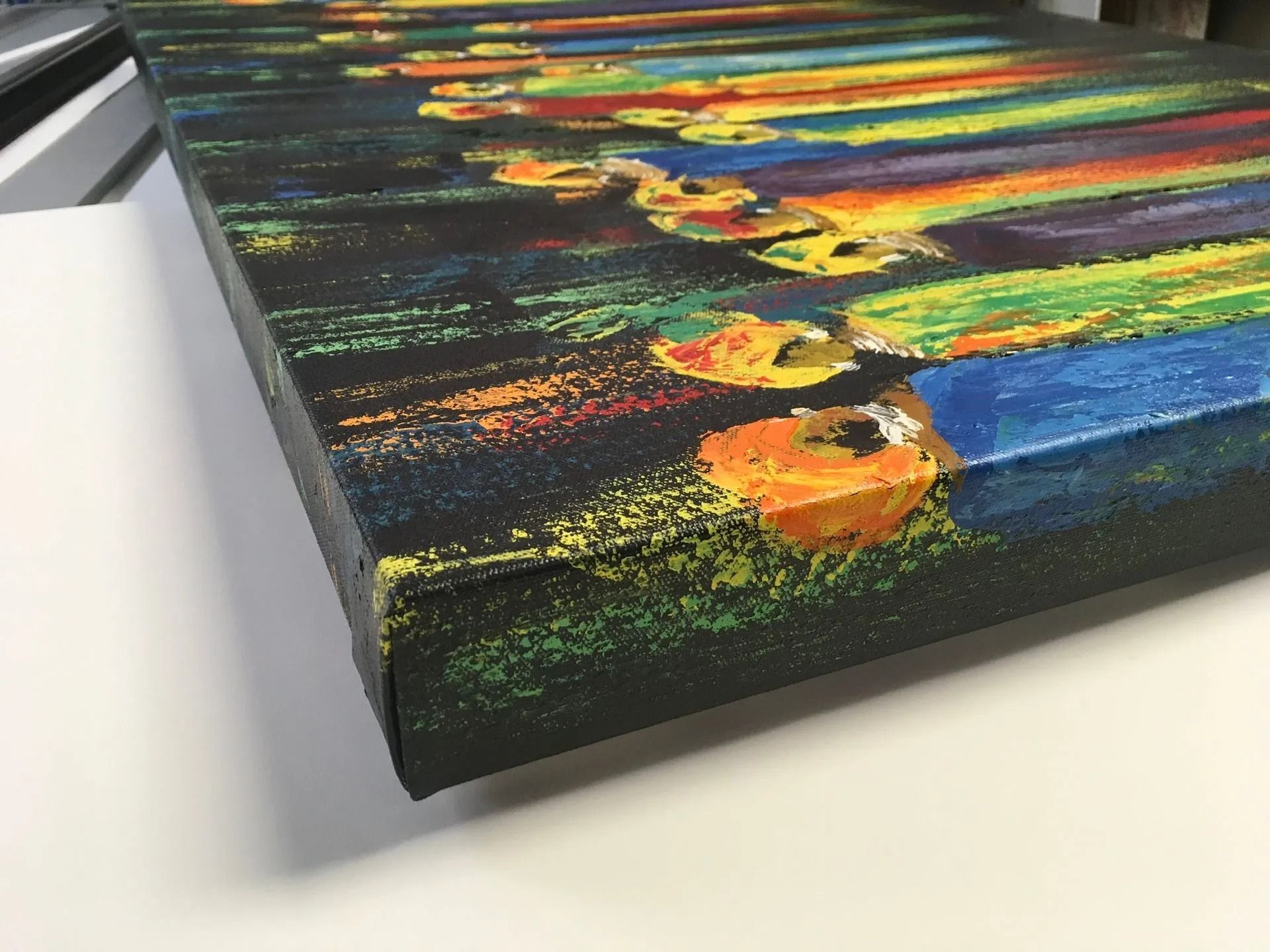 Colorful abstract painting on a black canvas, viewed at an angle on a white surface.