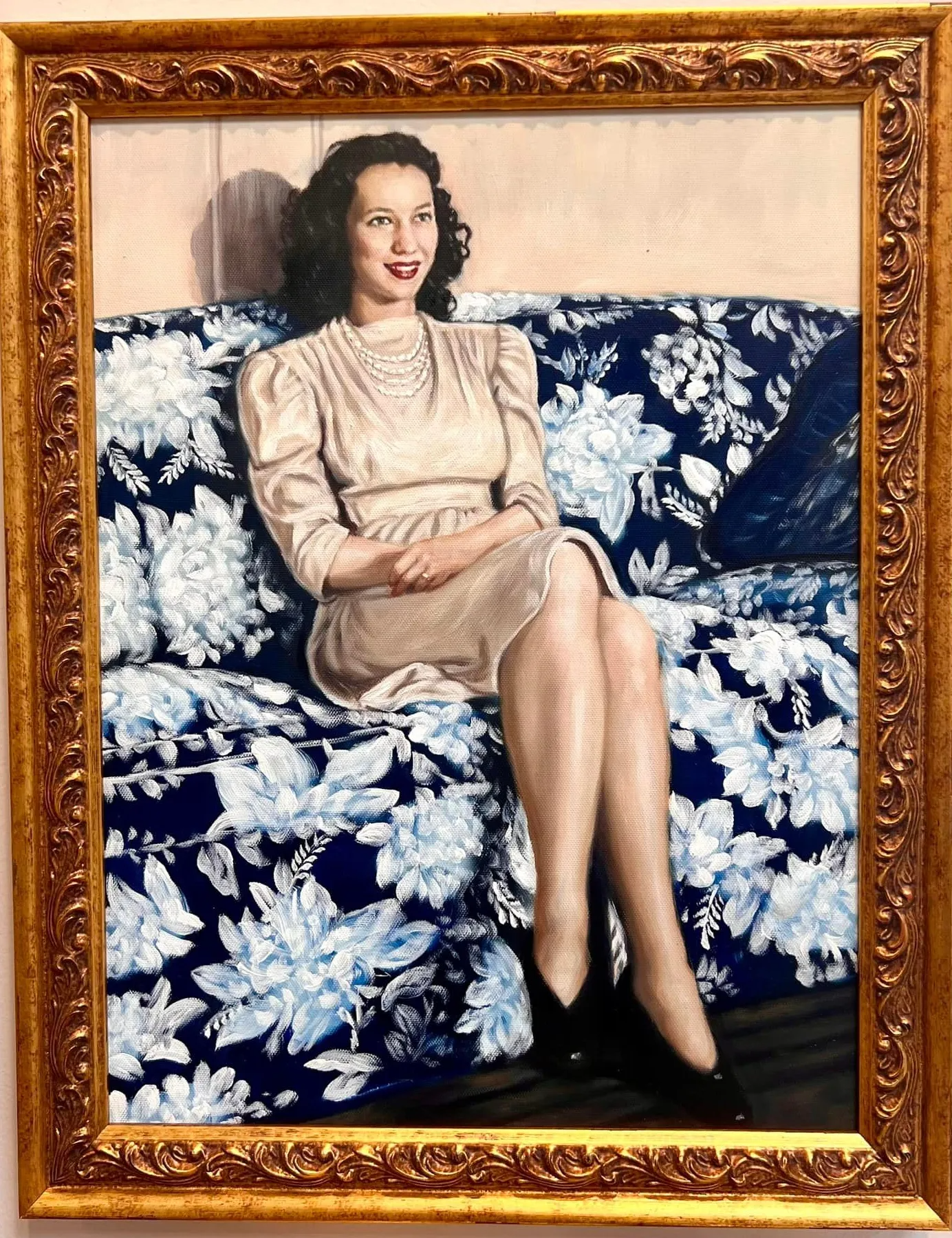 Portrait of a woman seated on a floral blue couch in a gold-framed painting