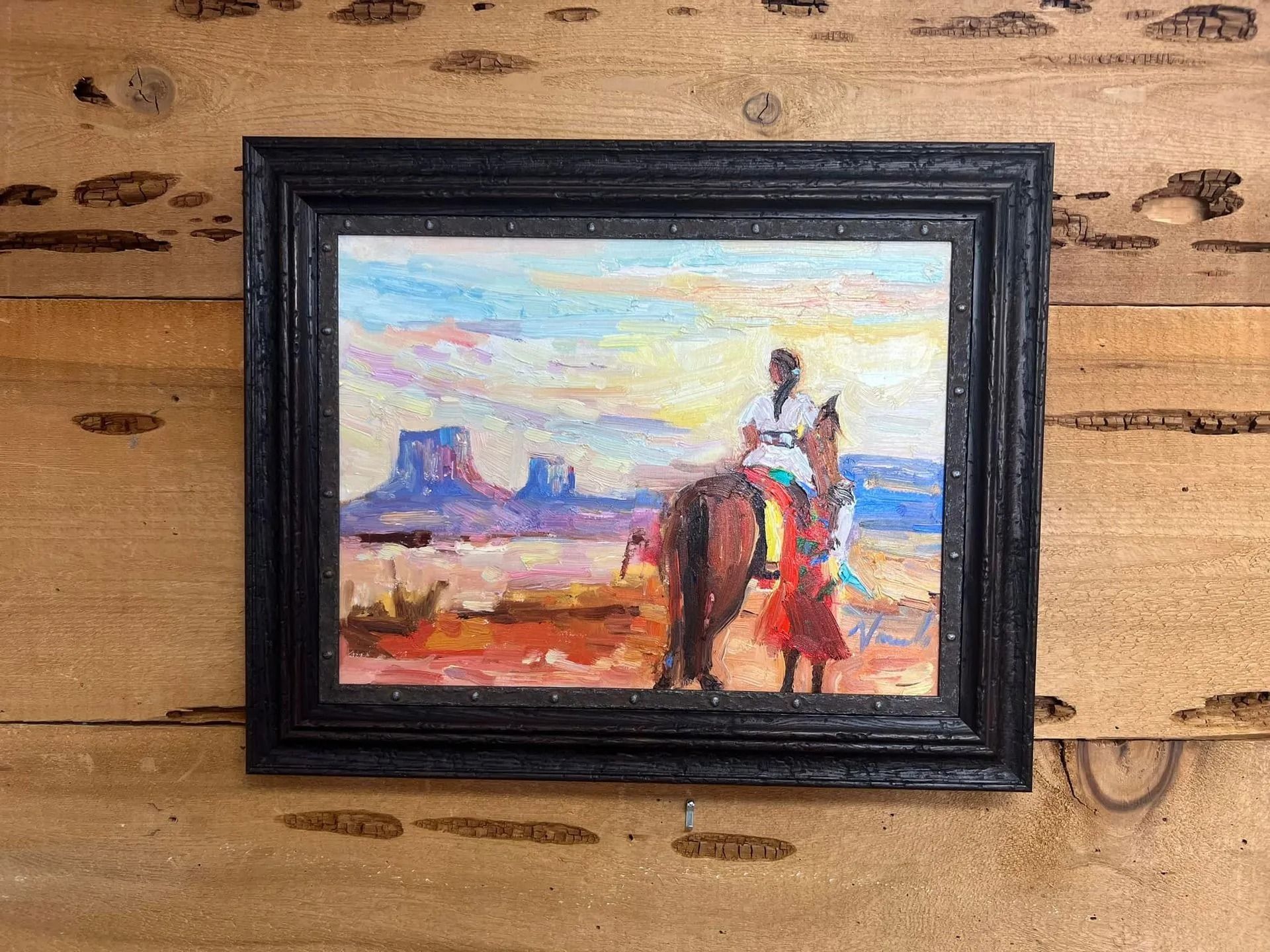 Framed painting of a cowboy on horseback in a desert landscape hanging on a wooden wall