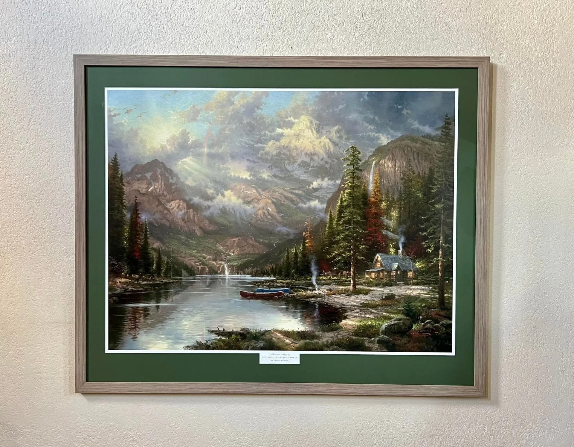 Framed landscape painting of a mountain lake with pine trees, snowy peaks, and a cloudy sky