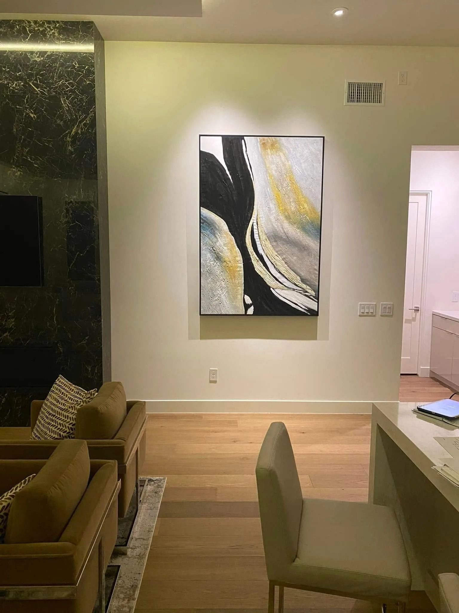 Modern living room with abstract wall art, beige seating, and open doorway to a bright room