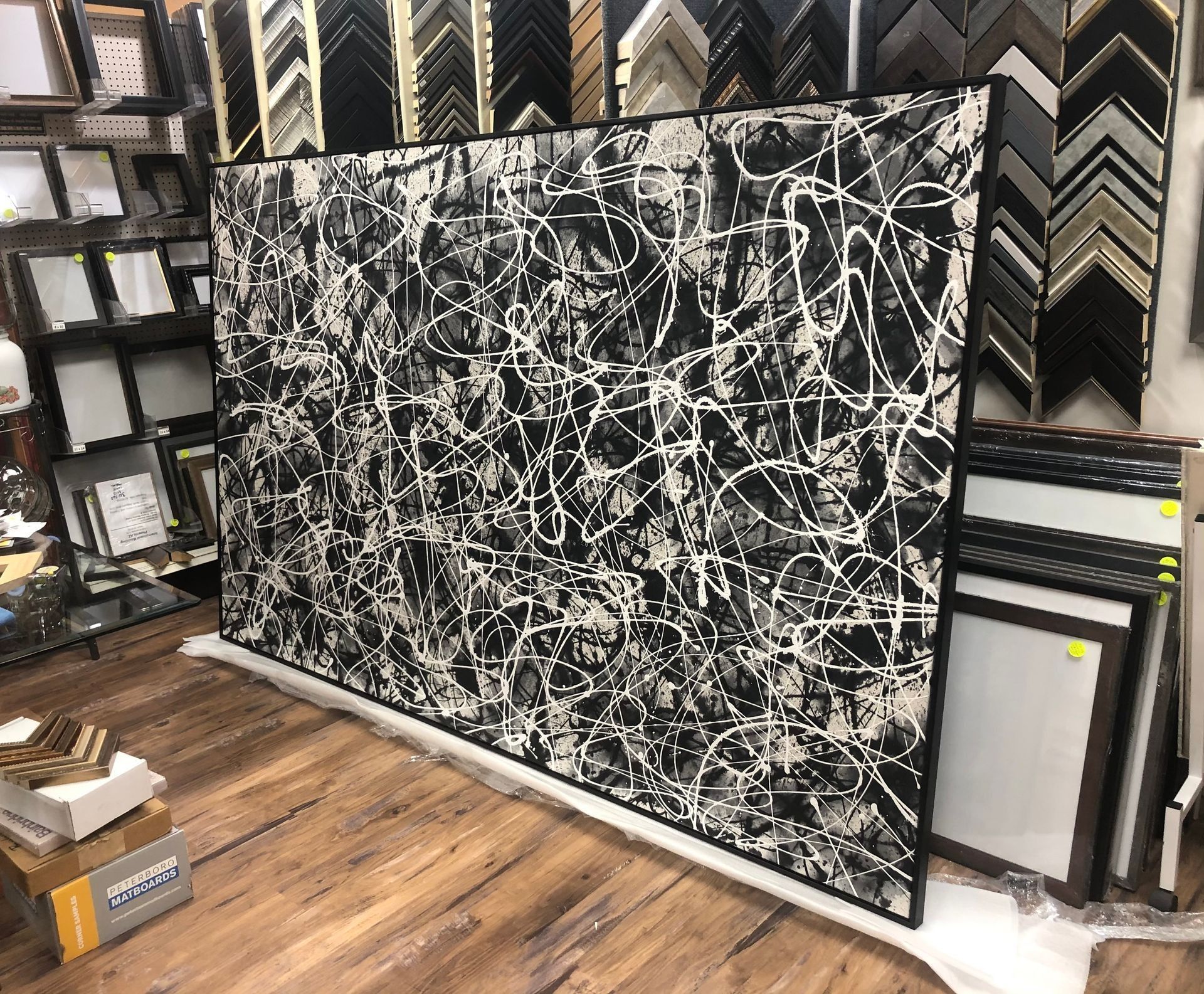 Black abstract painting with white splatters leaning in a framed art store display