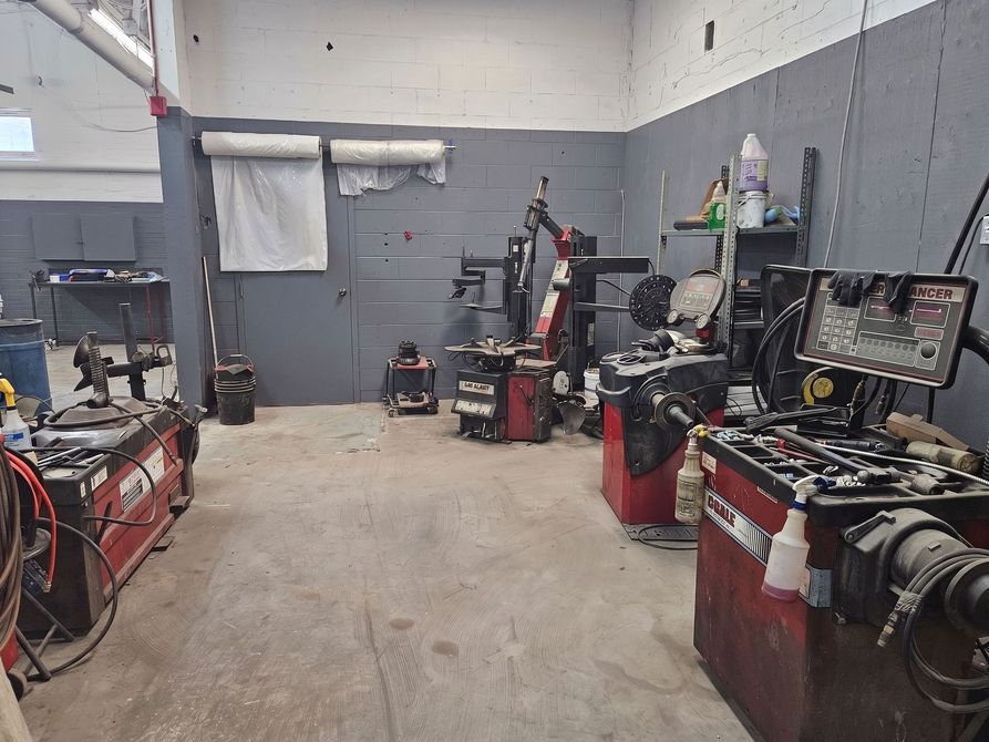 Intérieur d'un atelier de réparation automobile avec outils, pneus et armoires à outils rouges le long de murs gris.