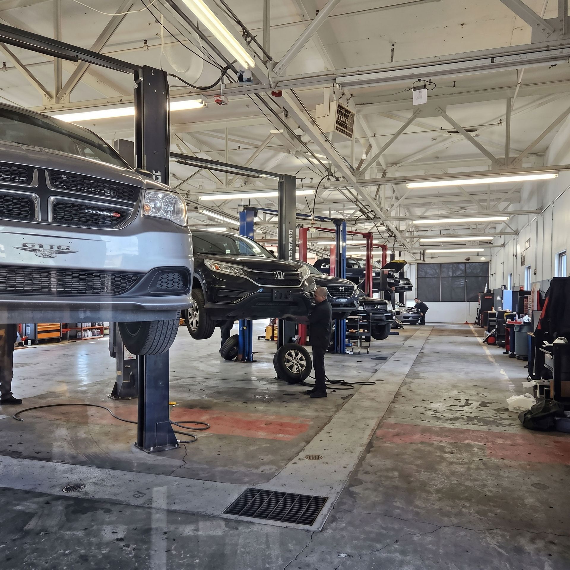 Atelier de réparation automobile avec plusieurs voitures surélevées sur des baies de service dans un garage industriel lumineux.