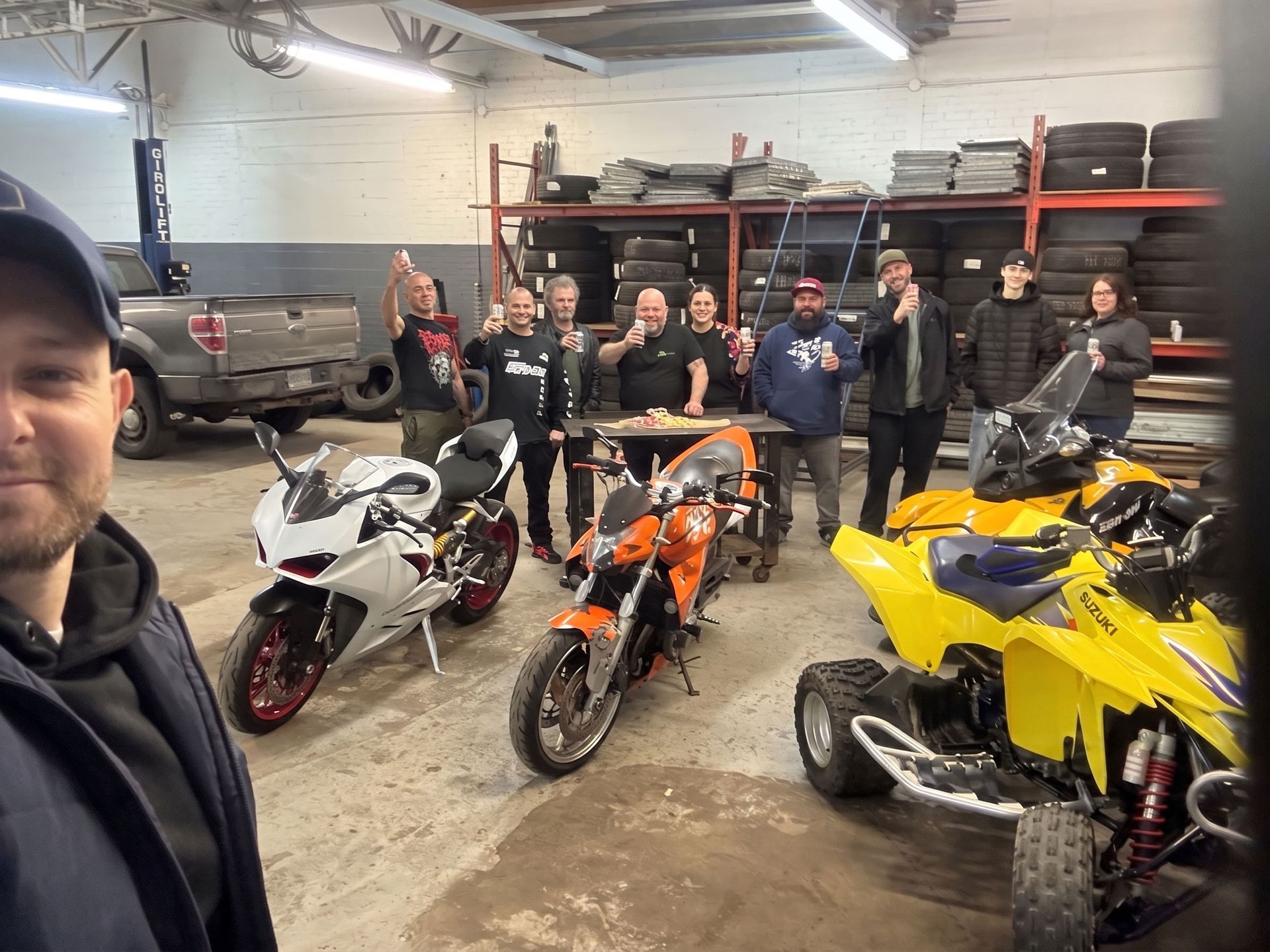Des personnes posent dans un garage avec trois motos sportives : blanche, orange et jaune.