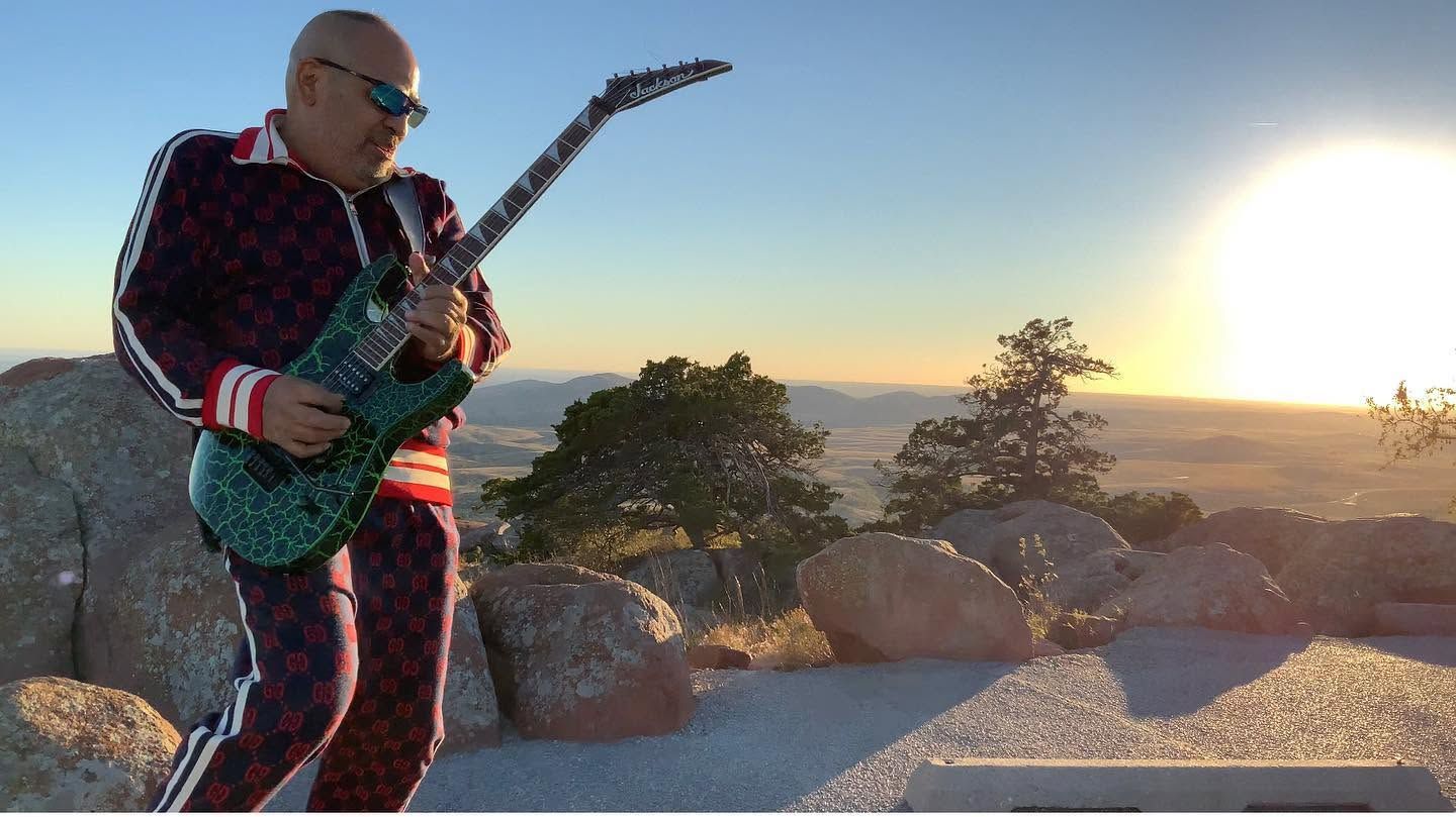 Musician playing green electric guitar outdoors at sunset with rocky desert landscape in the background