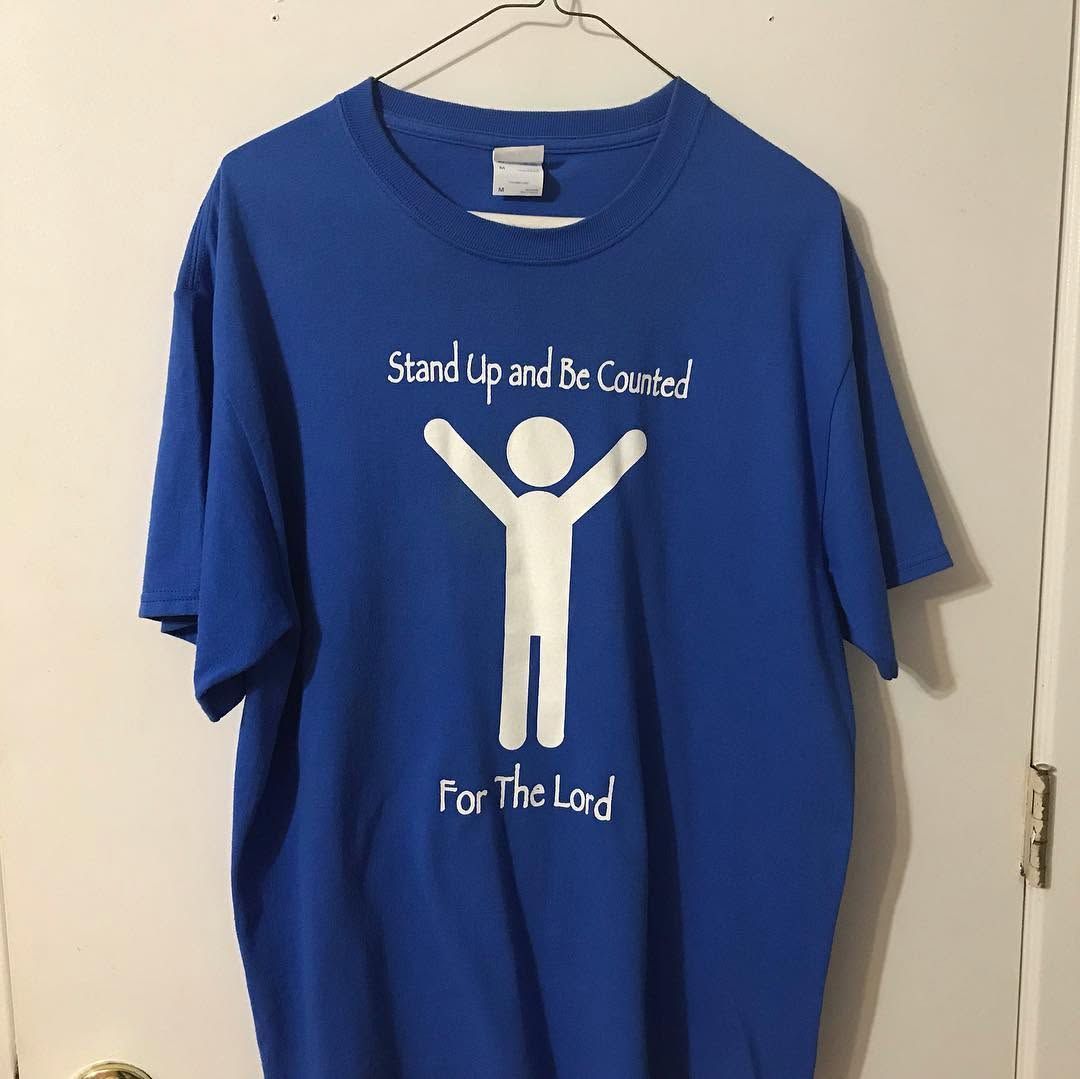 Blue T-shirt with a white figure and the words “Stand Up and Be Counted” and “For The Lord” hanging on a door