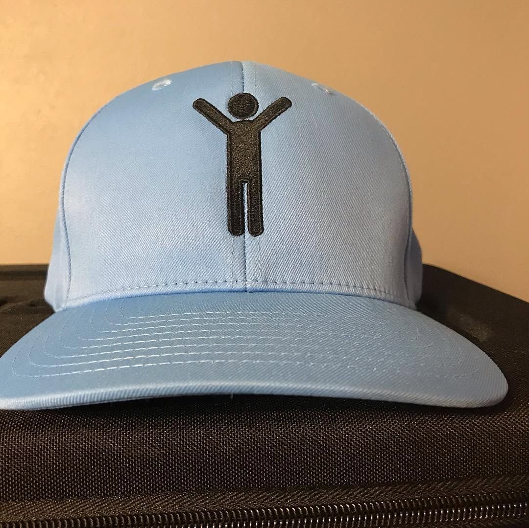 Light blue baseball cap with a black figure logo on the front, resting on a chair.