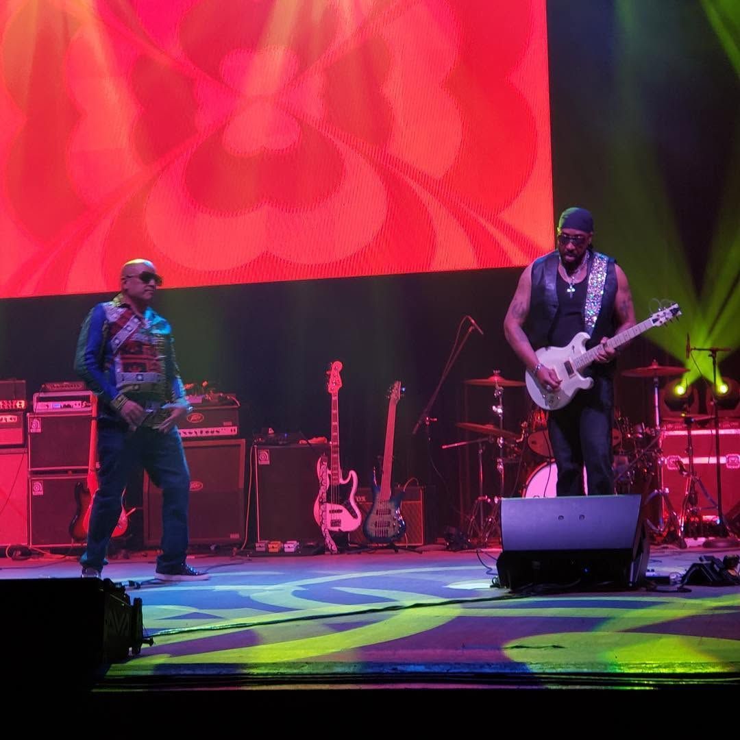 Two musicians performing on a red-lit stage with guitars and amplifiers