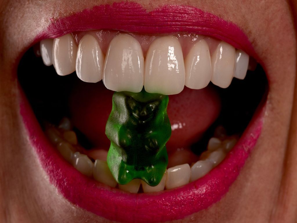 A woman is eating a green gummy bear in her mouth. Dentist Littleton CO