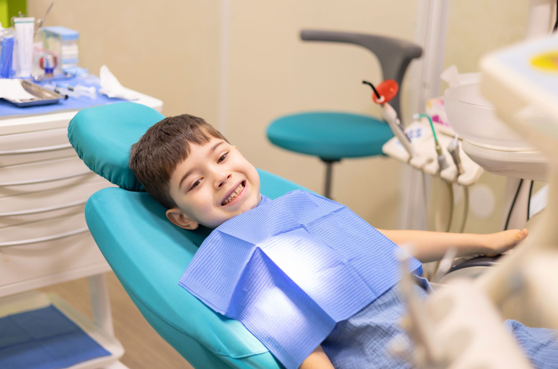 A young boy is sitting in a dental chair and smiling.