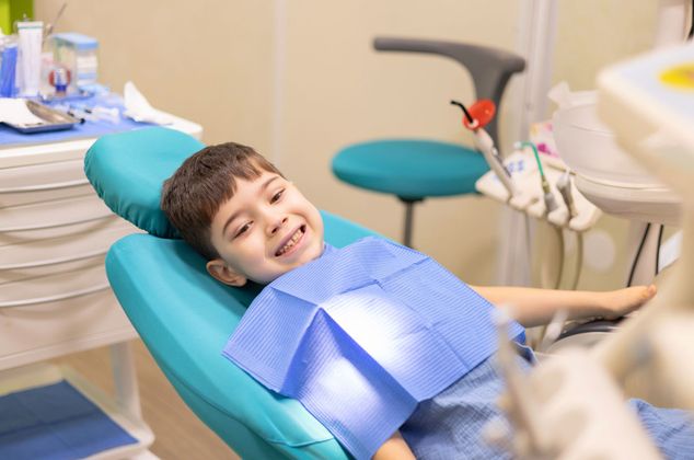 A young boy is sitting in a dental chair and smiling.